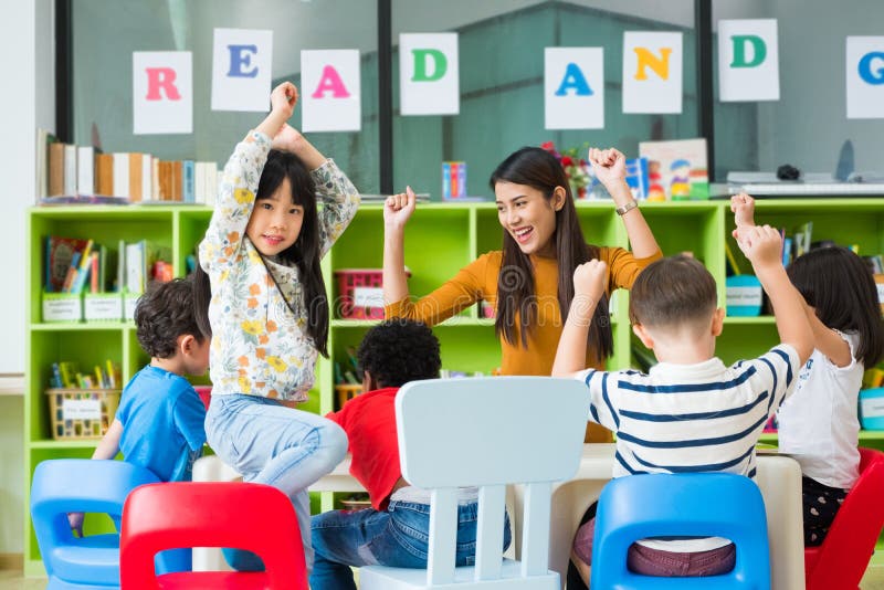 Szczęśliwy Azjatycki żeński nauczyciel i mieszający biegowi dzieciaki w sali lekcyjnej, dziecina przedszkolny pojęcie