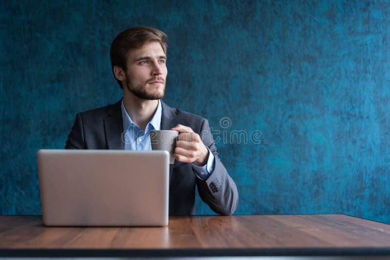 Szczęśliwy młody biznesmen używa laptop przy jego biurowym biurkiem obraz stock Szczęśliwy młody biznesmen używa laptop przy jego biurowym biurkiem obraz stock