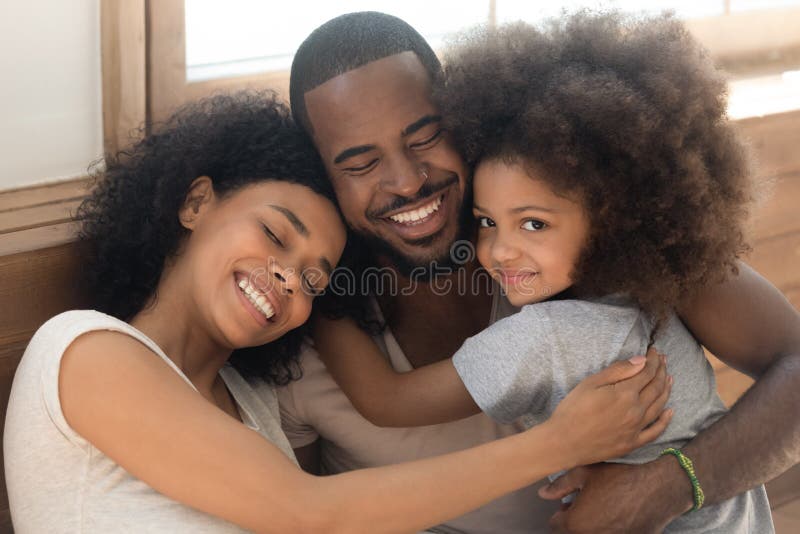 Happy african American young couple with preschooler sit hug posing looking at camera, loving biracial millennial parents with cute little daughter cuddle embrace enjoying tender moment at together. Happy african American young couple with preschooler sit hug posing looking at camera, loving biracial millennial parents with cute little daughter cuddle embrace enjoying tender moment at together