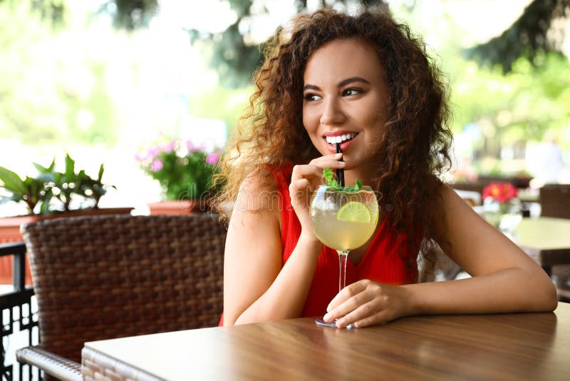 Happy African-American woman with glass of natural lemonade in cafe. Detox drink. Happy African-American woman with glass of natural lemonade in cafe. Detox drink