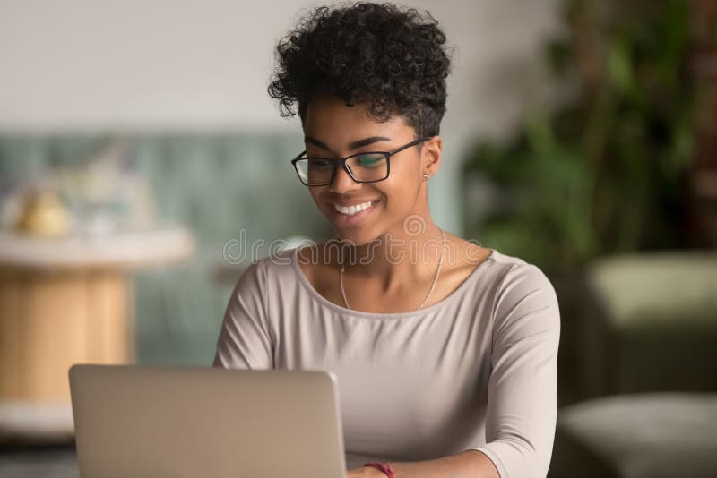 Szczęśliwa amerykanin afrykańskiego pochodzenia kobieta używa laptop pracy naukę w biurze