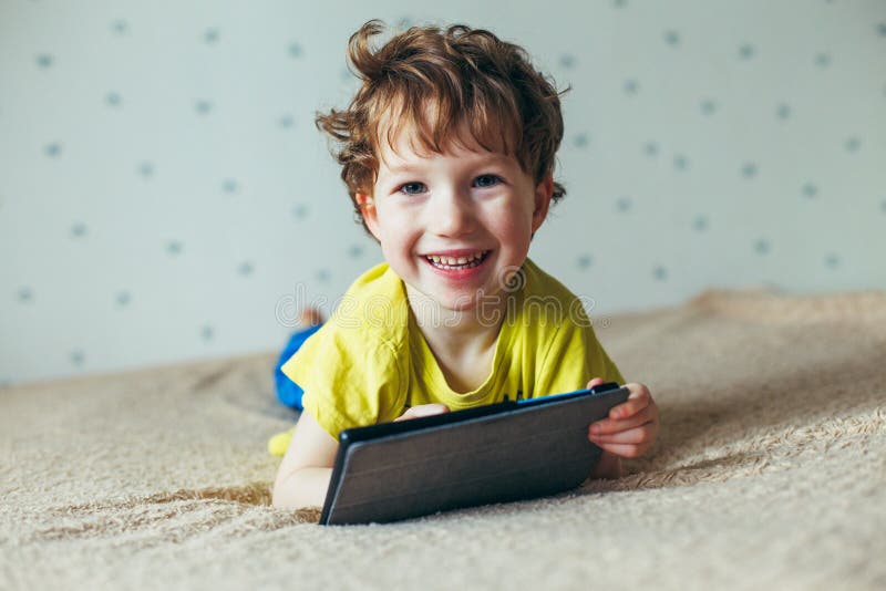 Szczęśliwa berbeć chłopiec ma zabawę bawić się grę na gadżecie, Preschool dzieciaka sititng na kanapie z uśmiechniętą twarzy dopa zdjęcia stock Szczęśliwa berbeć chłopiec ma zabawę bawić się grę na gadżecie, Preschool dzieciaka sititng na kanapie z uśmiechniętą twarzy dopa zdjęcia stock