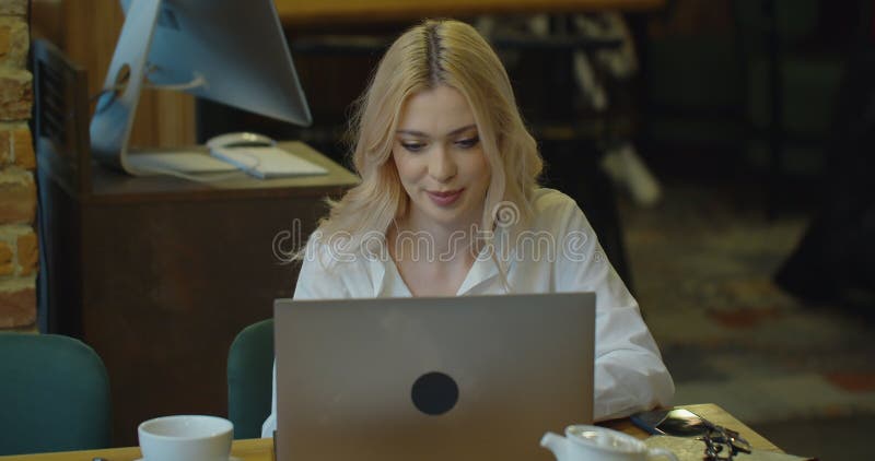 Szczęśliwa kobieta, pijąca kawę na komputerze przenośnym siedząca przy stoliku w kawiarni na pilocie, ucząca się w szkole lub prac