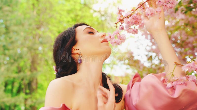 Szczęśliwa kobieta wdycha aromatowe różowe kwiaty sakura płatki upadają ręką dotykając gałęzi zbiory
