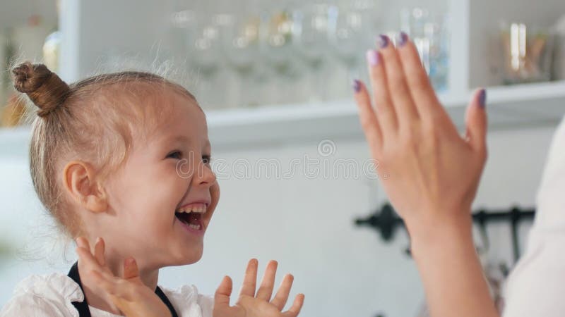 Szczęśliwa mała dziewczynka z jej macierzystym klaśnięciem ich ręki w kuchni fotografia stock Szczęśliwa mała dziewczynka z jej macierzystym klaśnięciem ich ręki w kuchni fotografia stock