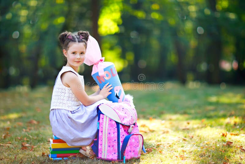 Happy little kid girl with backpack or satchel, books and big school bag or cone traditional in Germany for the first day of school. Healthy adorable child outdoors, in green park. Elementary class. Happy little kid girl with backpack or satchel, books and big school bag or cone traditional in Germany for the first day of school. Healthy adorable child outdoors, in green park. Elementary class