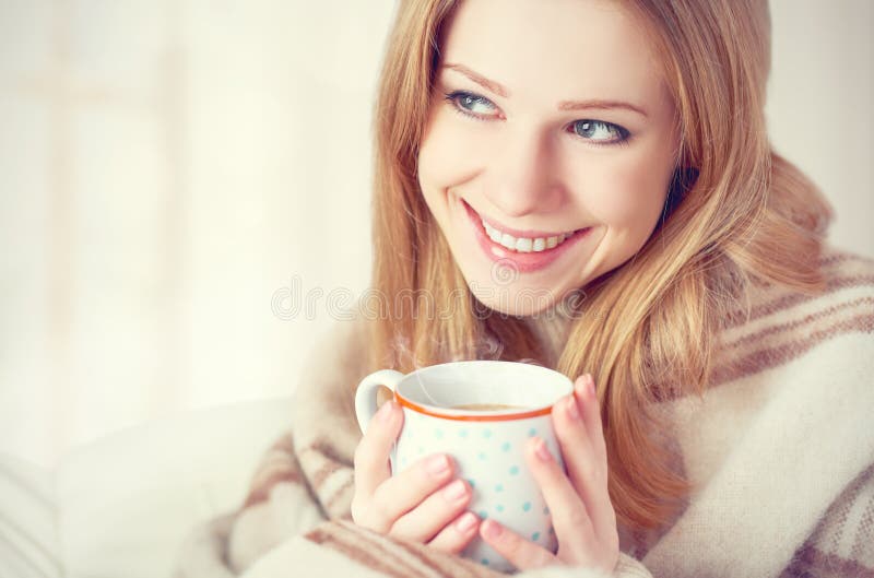 Szczęśliwa młoda kobieta jest pod filiżanką kawy na zima ranku i koc w domu