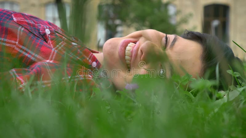 Szczęśliwa młoda kobieta kłama na trawie z pięknym uśmiechem z zębami, pogodny piękny natura dzień outdoors