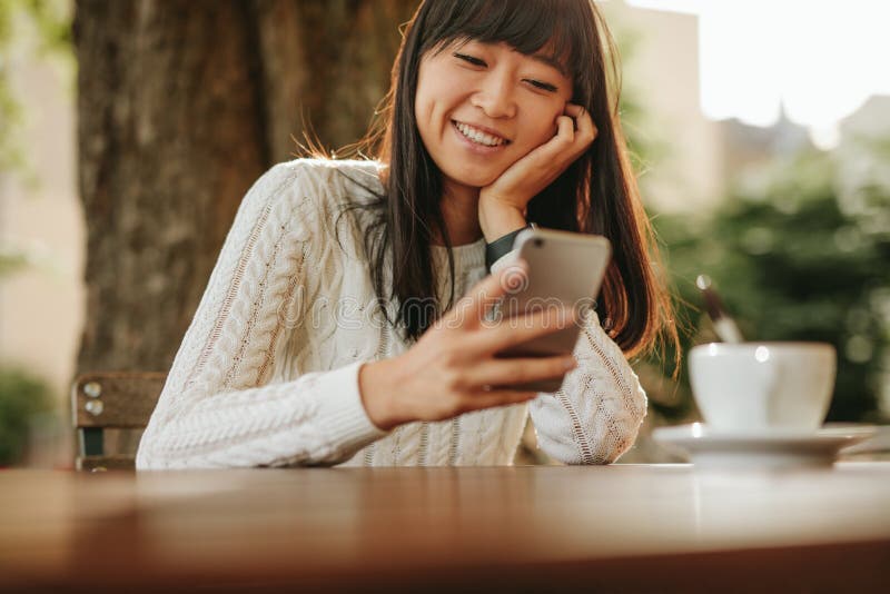 Szczęśliwa młoda kobieta używa jej telefon komórkowego przy kawiarnią fotografia royalty free