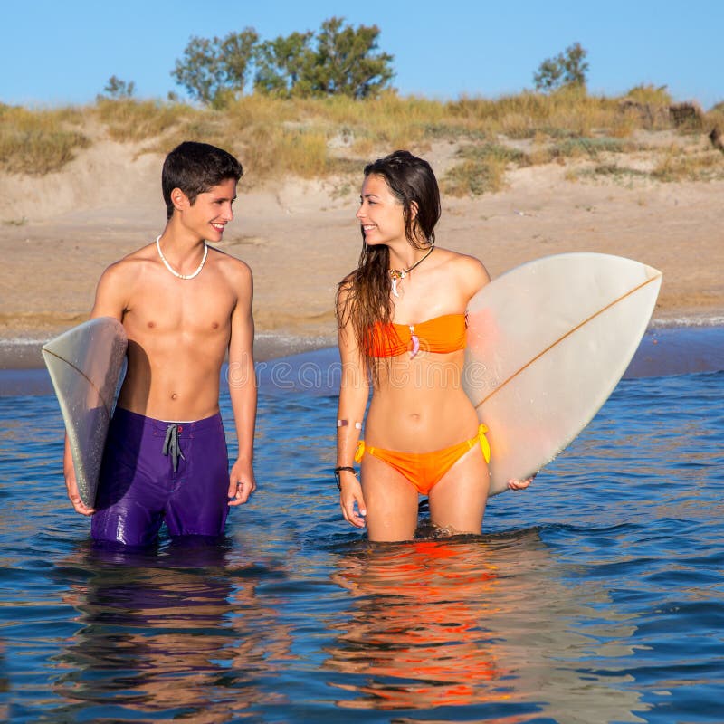 Szczęśliwa nastolatka surfingowa para na plażowym brzeg zdjęcie stock Szczęśliwa nastolatka surfingowa para na plażowym brzeg zdjęcie stock