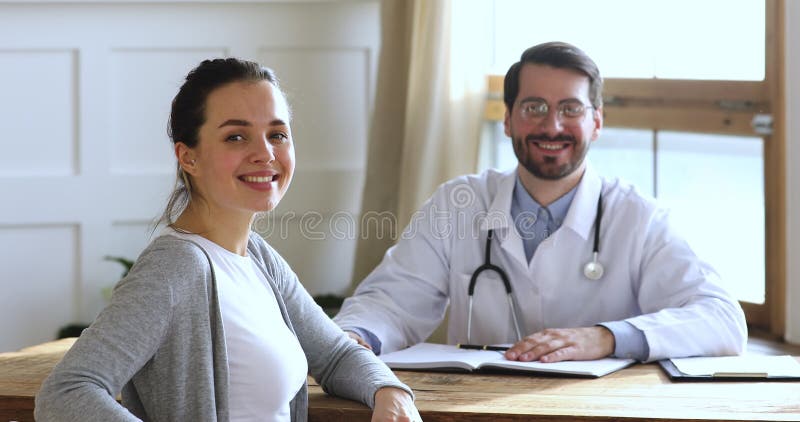 Szczęśliwa pacjentka siedząca przy stole z uśmiechniętym lekarzem ogólnym.