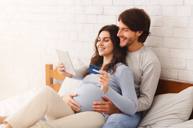 Szczęśliwa para czekająca na dziecko i robiąca zakupy online w łóżku w domu