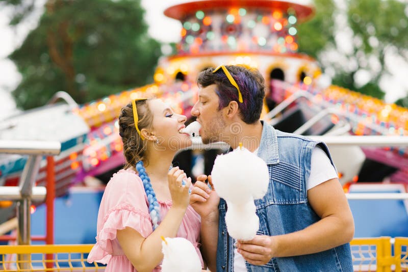 Happy couple in love enjoying each other in an amusement park. A guy and a girl eating cotton candy and laughing. Happy couple in love enjoying each other in an amusement park. A guy and a girl eating cotton candy and laughing.