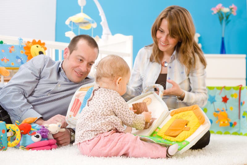 Happy family playing together: mother, father and 1 year old baby girl sitting on floor at children's room, smiling. Toys are officially property released. Happy family playing together: mother, father and 1 year old baby girl sitting on floor at children's room, smiling. Toys are officially property released.