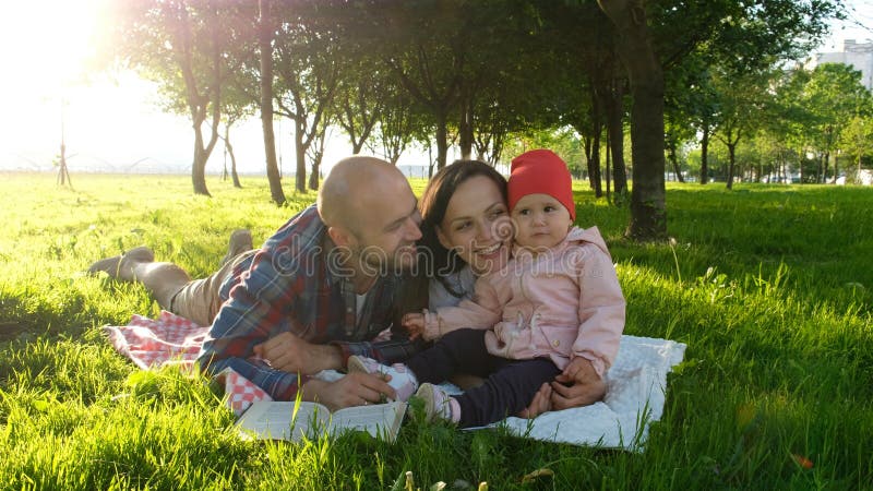Szczęśliwa rodzina ma odpoczynek i całuje w naturze z dzieckiem przy zmierzchem w parku Ojców buziaków matka zdjęcia stock Szczęśliwa rodzina ma odpoczynek i całuje w naturze z dzieckiem przy zmierzchem w parku Ojców buziaków matka zdjęcia stock