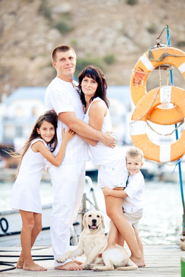 Happy young family in white clothing have fun and play with beautiful dog at vacations on berth in summer. Happy young family in white clothing have fun and play with beautiful dog at vacations on berth in summer