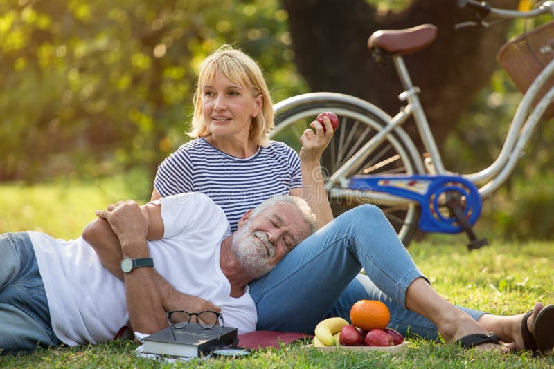 Happy senior couple relaxing in park  together. old people sitting on grass in the summer park . Elderly resting .mature relationships. women eating apple . men lying down or sleep on her knee or leg book fun romantic pensioner retirement romance adult aged autumn caucasian family female fruit healthy husband leisure lifestyle love natural nature older outdoors outside picnic pleasure recreational relaxation retired smile trust two wife. Happy senior couple relaxing in park  together. old people sitting on grass in the summer park . Elderly resting .mature relationships. women eating apple . men lying down or sleep on her knee or leg book fun romantic pensioner retirement romance adult aged autumn caucasian family female fruit healthy husband leisure lifestyle love natural nature older outdoors outside picnic pleasure recreational relaxation retired smile trust two wife