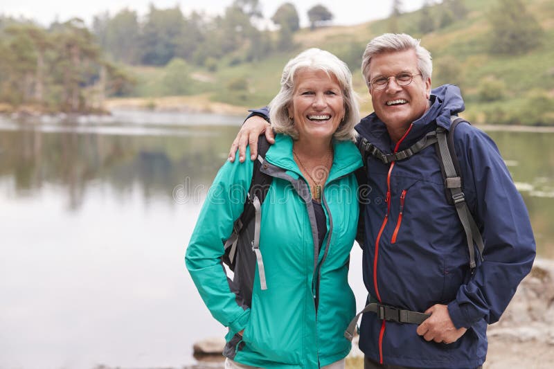 Szczęśliwa starsza pary pozycja na brzeg jezioro ono uśmiecha się kamera, Jeziorny okręg, UK