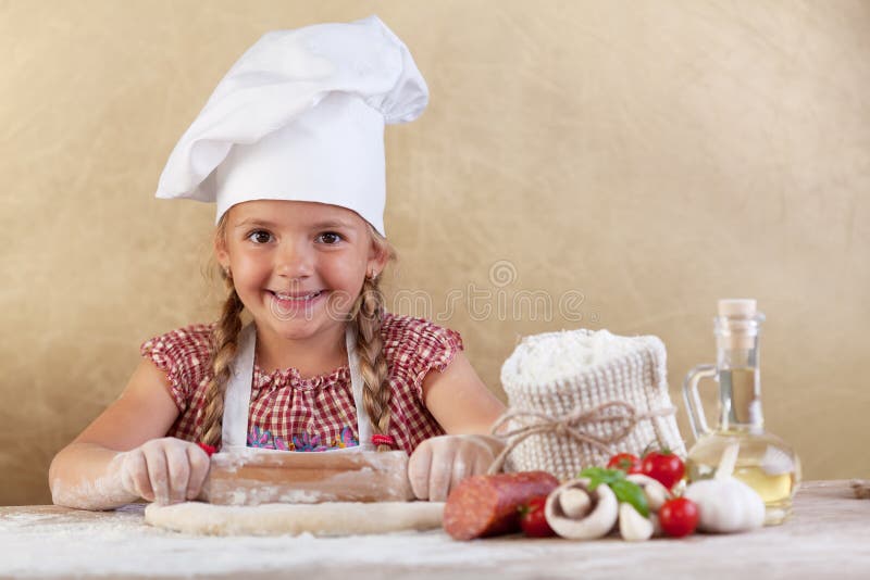 Szczęśliwa szef kuchni mała dziewczynka rozciąga ciasto obrazy stock Szczęśliwa szef kuchni mała dziewczynka rozciąga ciasto obrazy stock