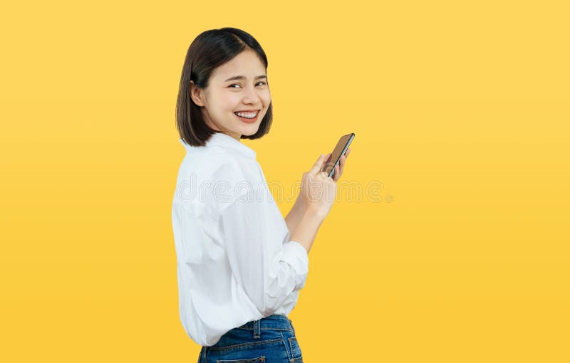 Szczęśliwa uśmiechnięta Azjatycka kobieta z trzymać mądrze telefon na żółtym tle fotografia royalty free Szczęśliwa uśmiechnięta Azjatycka kobieta z trzymać mądrze telefon na żółtym tle fotografia royalty free