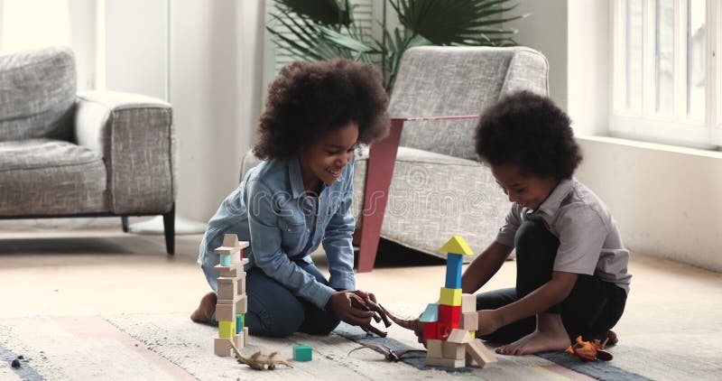 Szczęśliwe afrykańskie dzieci bawiące się w zabawki siedzące na podłodze w domu