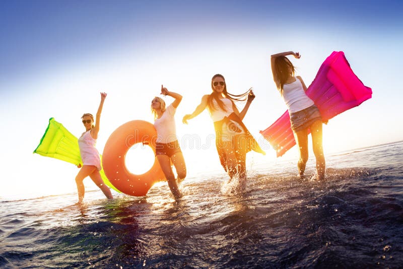 Happy girls are walking and having fun in sunset water surface with swimming mattresses. Happy girls are walking and having fun in sunset water surface with swimming mattresses