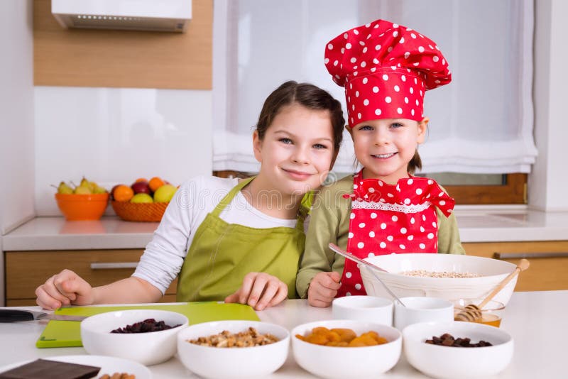 Happy girls sisters cooking together. Young happy children kids family having fun preparing granola in kitchen at home. Happy girls sisters cooking together. Young happy children kids family having fun preparing granola in kitchen at home