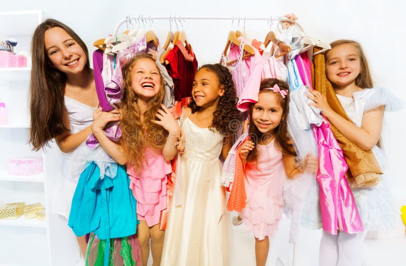 Happy girls during standing among hangers with colorful bright dresses and children clothes in the store. Happy girls during standing among hangers with colorful bright dresses and children clothes in the store