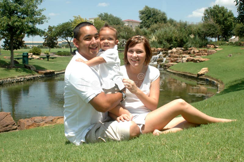 Young married couple with their toddler child. New family taking pictures in white shirts and tan shorts. Family of three. Young married couple with their toddler child. New family taking pictures in white shirts and tan shorts. Family of three.