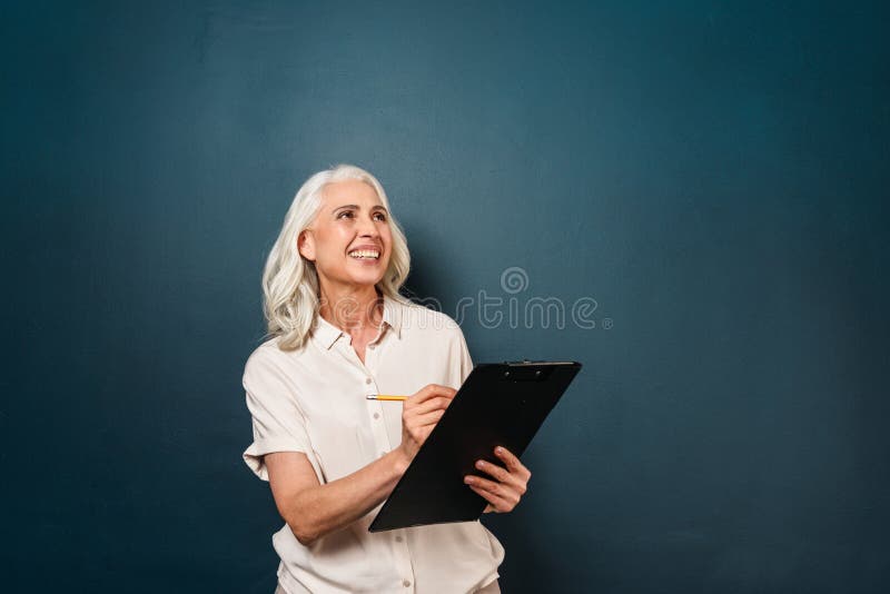 Szczęśliwe uśmiechnięte dojrzałe starej kobiety writing notatki w schowku zdjęcie stock Szczęśliwe uśmiechnięte dojrzałe starej kobiety writing notatki w schowku zdjęcie stock