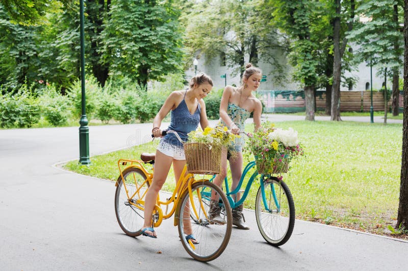 Szczęśliwego boho modne dziewczyny jadą wpólnie na bicyklach w parku zdjęcie royalty free Szczęśliwego boho modne dziewczyny jadą wpólnie na bicyklach w parku zdjęcie royalty free