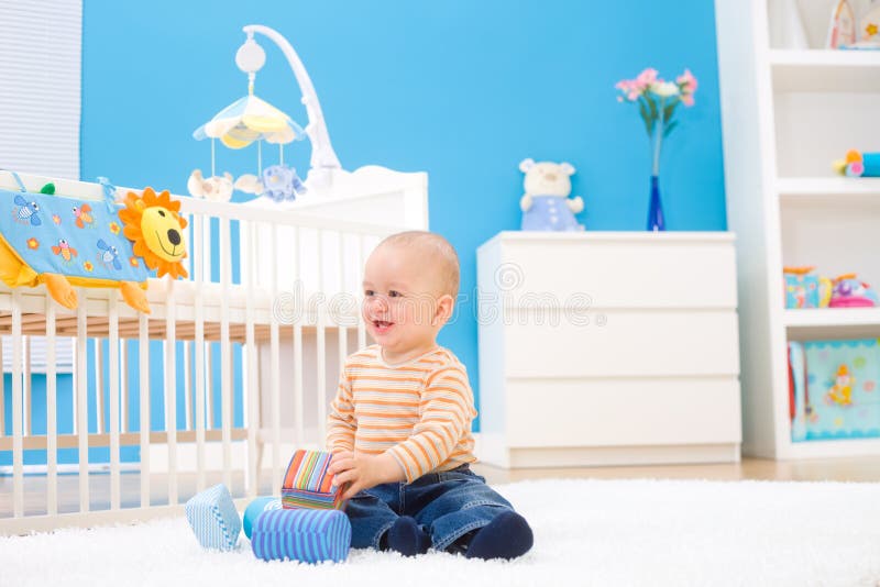 Happy baby boy (1 year old) sitting on floor at children's room and playing with toy blocks. Toys are officially property released. Happy baby boy (1 year old) sitting on floor at children's room and playing with toy blocks. Toys are officially property released.