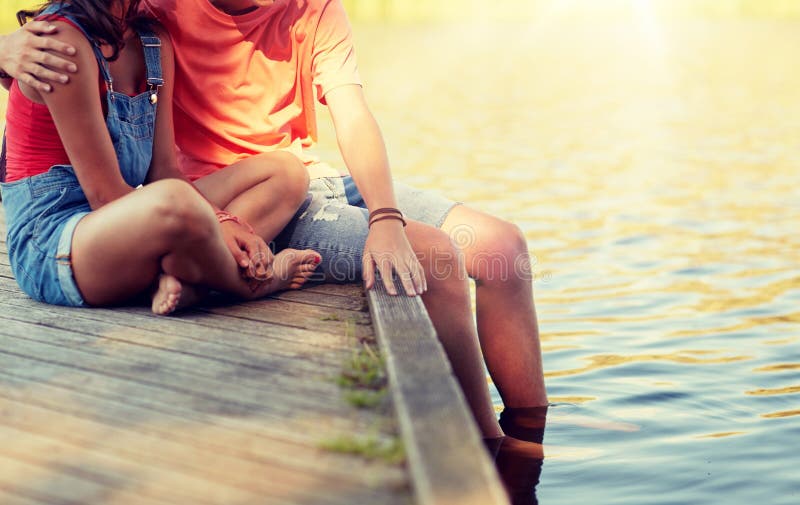 Holidays, vacation, love and people concept - happy teenage couple sitting on river berth at summer. Holidays, vacation, love and people concept - happy teenage couple sitting on river berth at summer