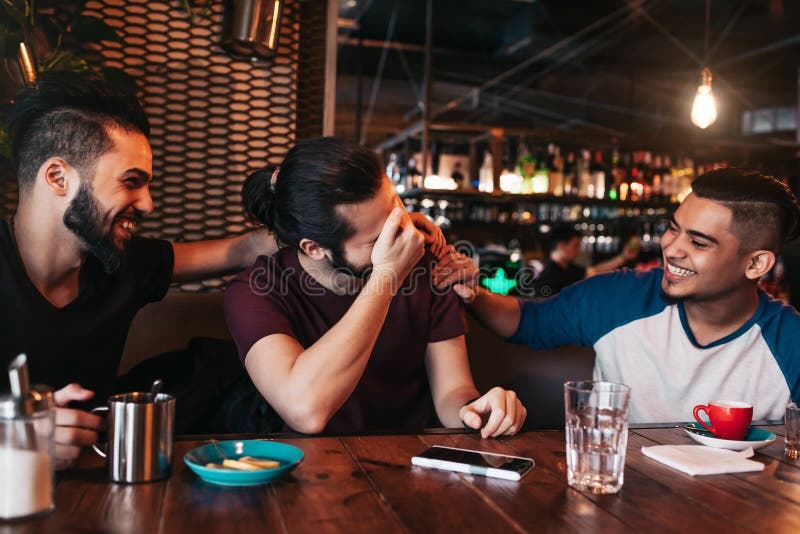 Happy arabic young men hanging in loft cafe. Group of mixed race people having fun in lounge bar. Friends chilling out and laughing. Happy arabic young men hanging in loft cafe. Group of mixed race people having fun in lounge bar. Friends chilling out and laughing