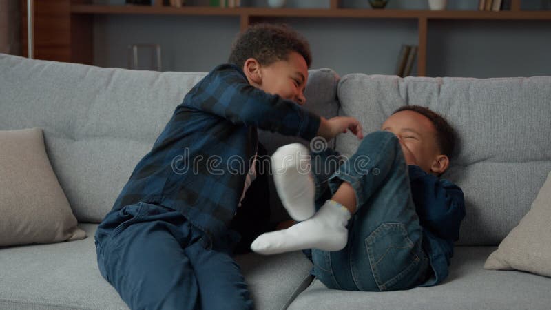 Szczęśliwi dwaj amerykańscy bracia przyjaciele małe dzieci chłopcy rodzeństwo na kanapie domowej śmiejący się z walki