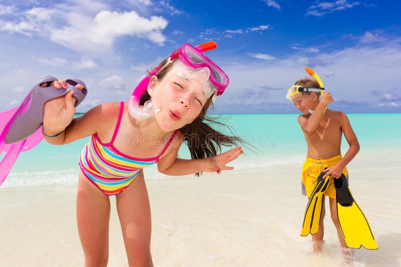 Happy young girl and boy with snorkeling equipment on sandy tropical beach, blue sky and cloudscape background. Happy young girl and boy with snorkeling equipment on sandy tropical beach, blue sky and cloudscape background.