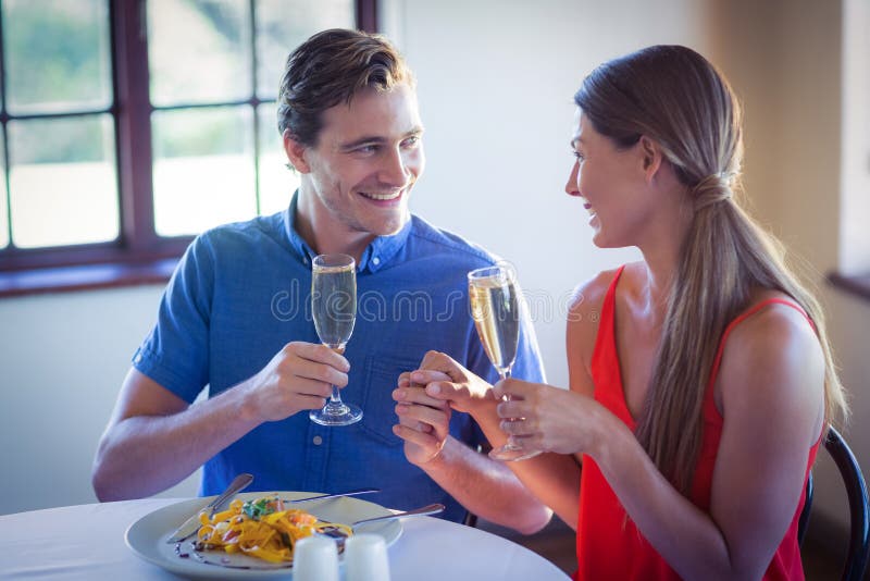Szczęśliwi potomstwa dobierają się wznosić toast szampańskich flety podczas gdy mieć lunch zdjęcie stock Szczęśliwi potomstwa dobierają się wznosić toast szampańskich flety podczas gdy mieć lunch zdjęcie stock