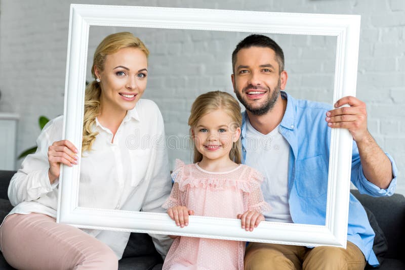 szczęśliwi rodzice z uroczą małą córką trzyma bielu ono uśmiecha się i ramę zdjęcia stock szczęśliwi rodzice z uroczą małą córką trzyma bielu ono uśmiecha się i ramę zdjęcia stock
