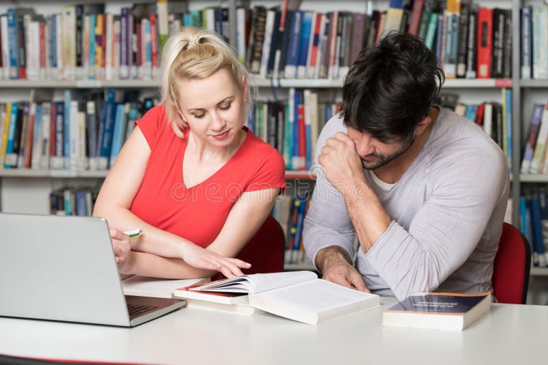 Szczęśliwi ucznie Pracuje Z laptopem W bibliotece zdjęcie stock Szczęśliwi ucznie Pracuje Z laptopem W bibliotece zdjęcie stock