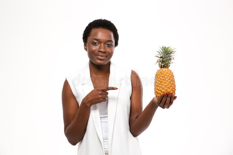 Szczęśliwy amerykanin afrykańskiego pochodzenia kobiety mienia ananas i wskazywać na nim zdjęcie stock Szczęśliwy amerykanin afrykańskiego pochodzenia kobiety mienia ananas i wskazywać na nim zdjęcie stock