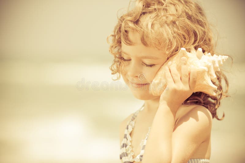 Szczęśliwy dziecko słucha seashell przy plażą
