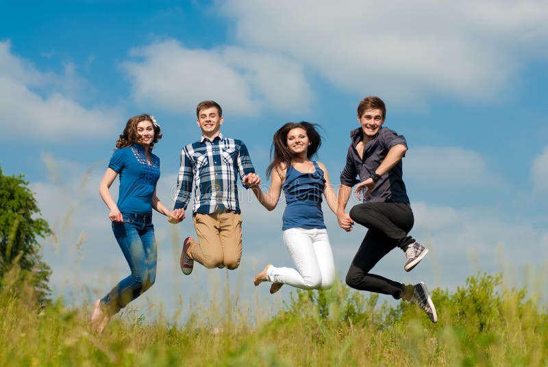 Portrait of Happy smiling mixed group of Young people two beautiful women and two handsome young men having fun outdoors on a bright sunny day of spring or summer joyfully jumping in excitement on the field of green grass and blue sky on the background. Portrait of Happy smiling mixed group of Young people two beautiful women and two handsome young men having fun outdoors on a bright sunny day of spring or summer joyfully jumping in excitement on the field of green grass and blue sky on the background