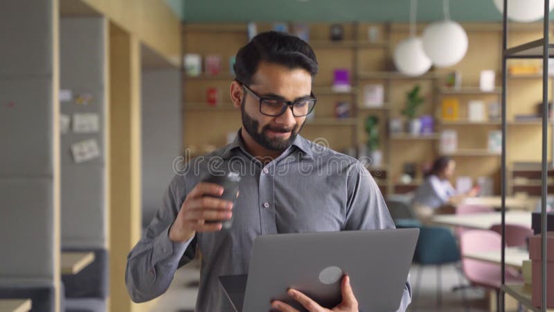 Szczęśliwy indiański biznesmen trzymający kawę i laptop chodzący do biura.