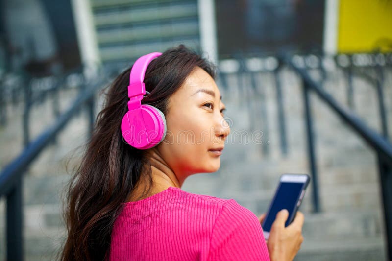 Szczęśliwy młody azjatykci kobiety szkolenie Jest s?uchaj?ca muzyka od s?uchawek i patrze? smartphone zdjęcie royalty free Szczęśliwy młody azjatykci kobiety szkolenie Jest s?uchaj?ca muzyka od s?uchawek i patrze? smartphone zdjęcie royalty free