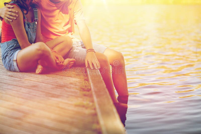 Holidays, vacation, love and people concept - happy teenage couple sitting on river berth at summer. Holidays, vacation, love and people concept - happy teenage couple sitting on river berth at summer