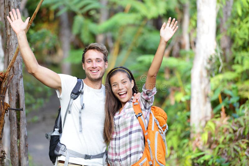 Happy hiking - hikers cheering joyful in forest. Cheerful excited hiker couple with arms raised up outstretched in joy smiling happy looking at camera. Multiethnic men and women on Big Island, Hawaii. Happy hiking - hikers cheering joyful in forest. Cheerful excited hiker couple with arms raised up outstretched in joy smiling happy looking at camera. Multiethnic men and women on Big Island, Hawaii.