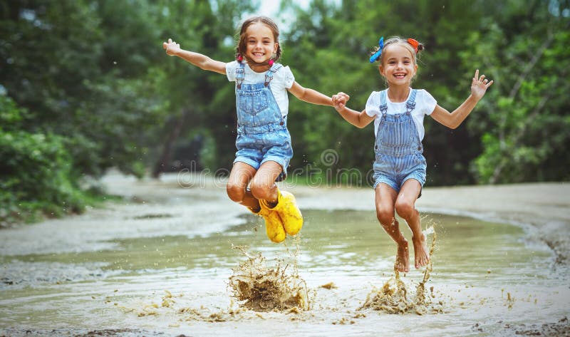 Szczęśliwy śmieszny siostra bliźniaków dziecka dziewczyny doskakiwanie na kałużach w pocieraniu