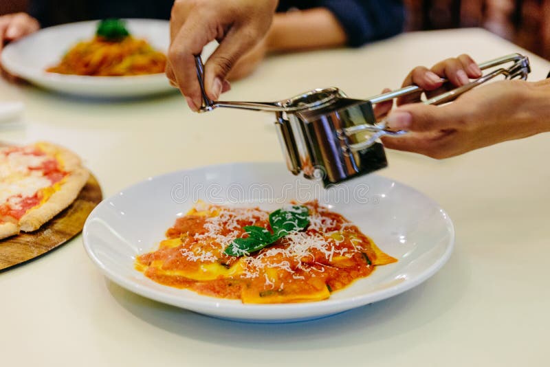 Szef kuchni ręki przecinania parmesan ser na pierożku z pomidorowym kumberlandem i basilem w bielu talerzu na białym tablecloth zdjęcia stock Szef kuchni ręki przecinania parmesan ser na pierożku z pomidorowym kumberlandem i basilem w bielu talerzu na białym tablecloth zdjęcia stock