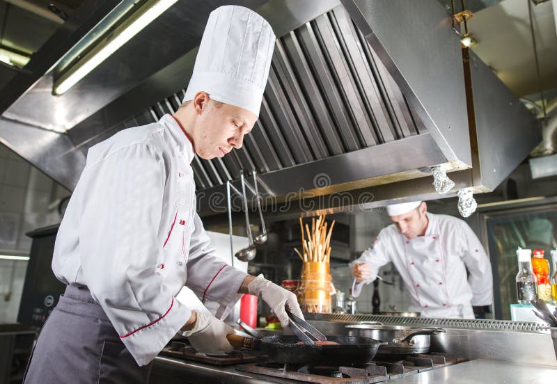 Szef kuchni w restauracyjnej kuchni przy kuchenką z niecką, gotuje zdjęcia stock Szef kuchni w restauracyjnej kuchni przy kuchenką z niecką, gotuje zdjęcia stock