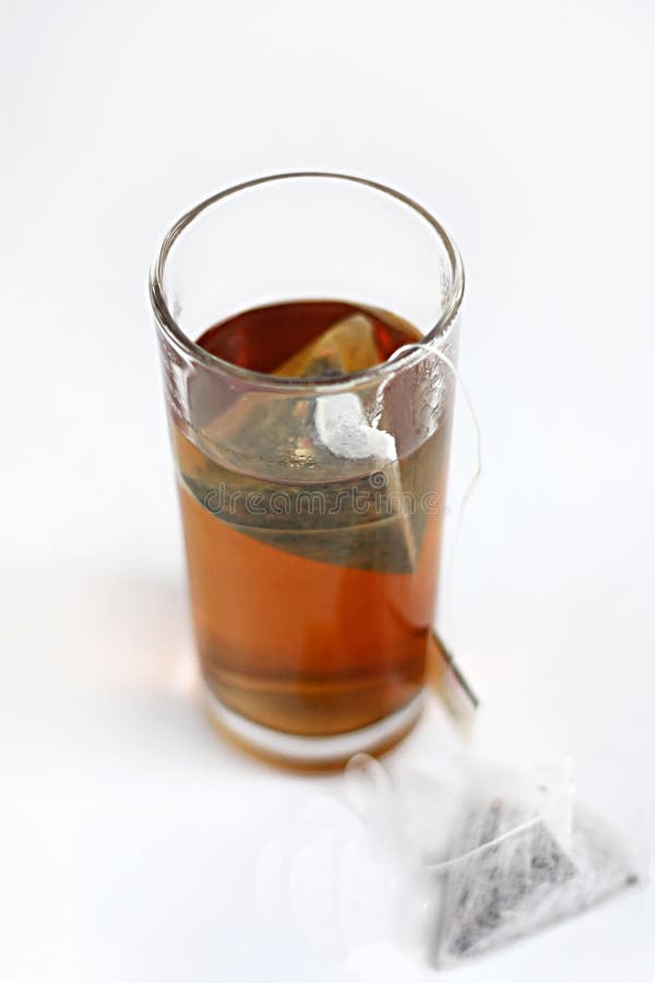 Black tea in a glass with piramid teabag on a side on white background. Black tea in a glass with piramid teabag on a side on white background